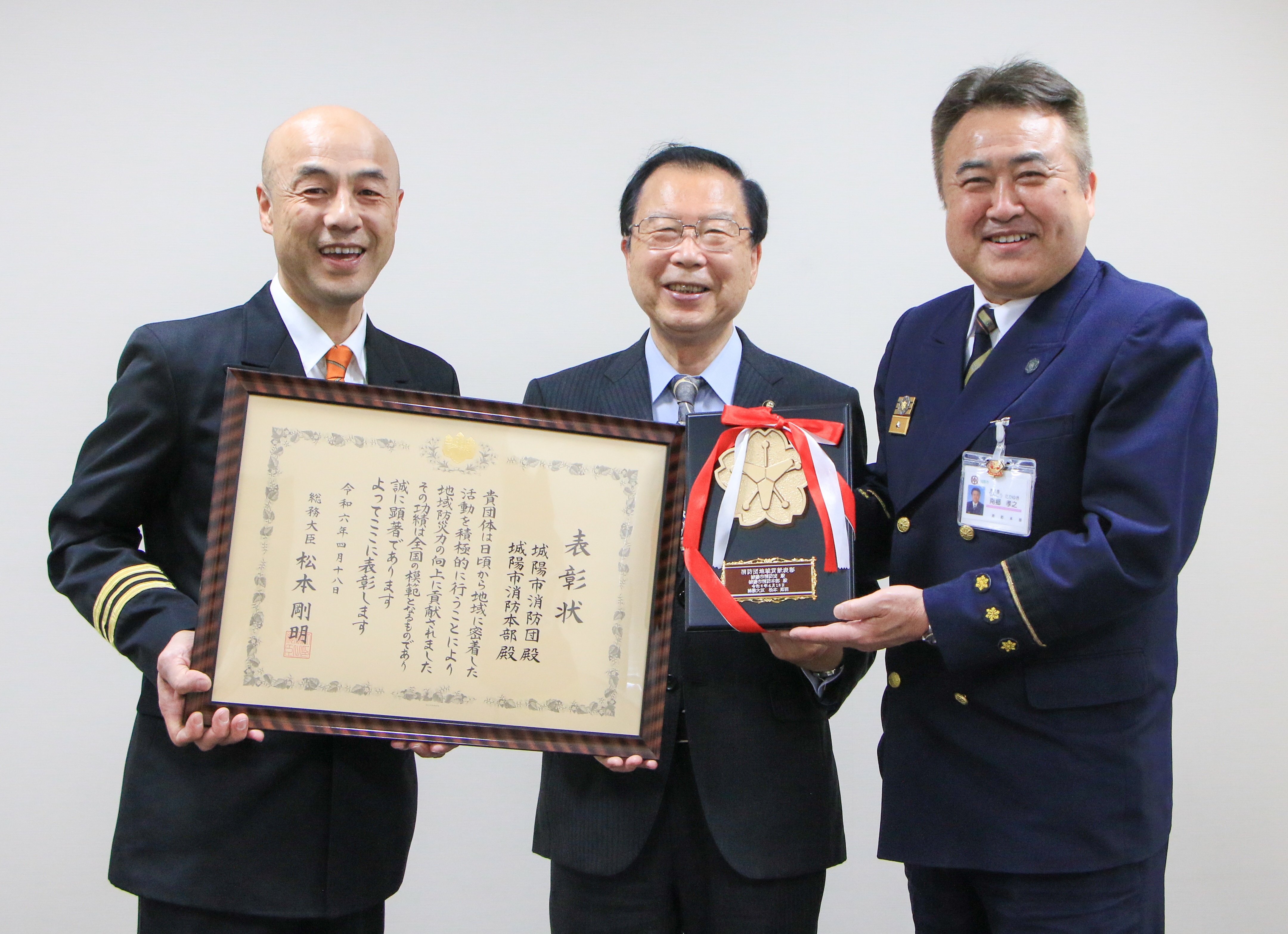 総務大臣からの表彰状と盾を手に笑顔の消防団長、消防長、市長
